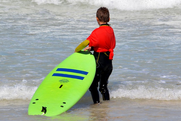 child standing at the edge of the ocean holding a body surfing board